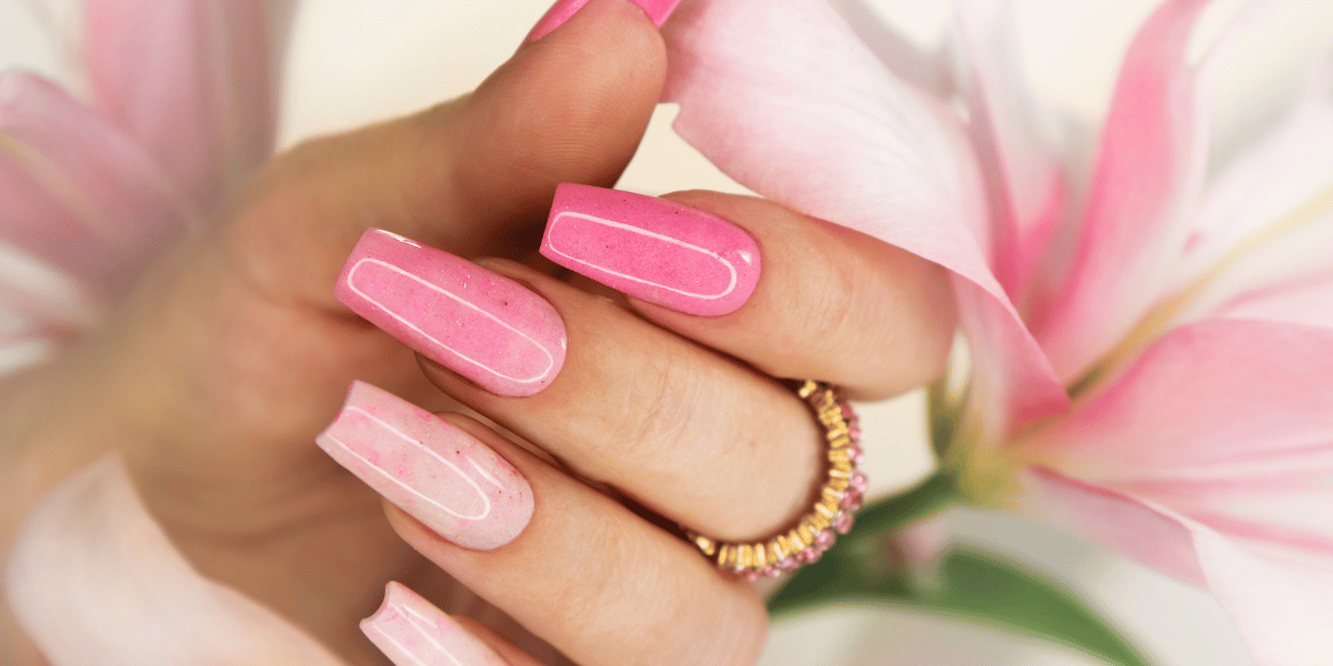 Pink glossy long nails with white outline accents, featuring a soft floral background and a gold ring.