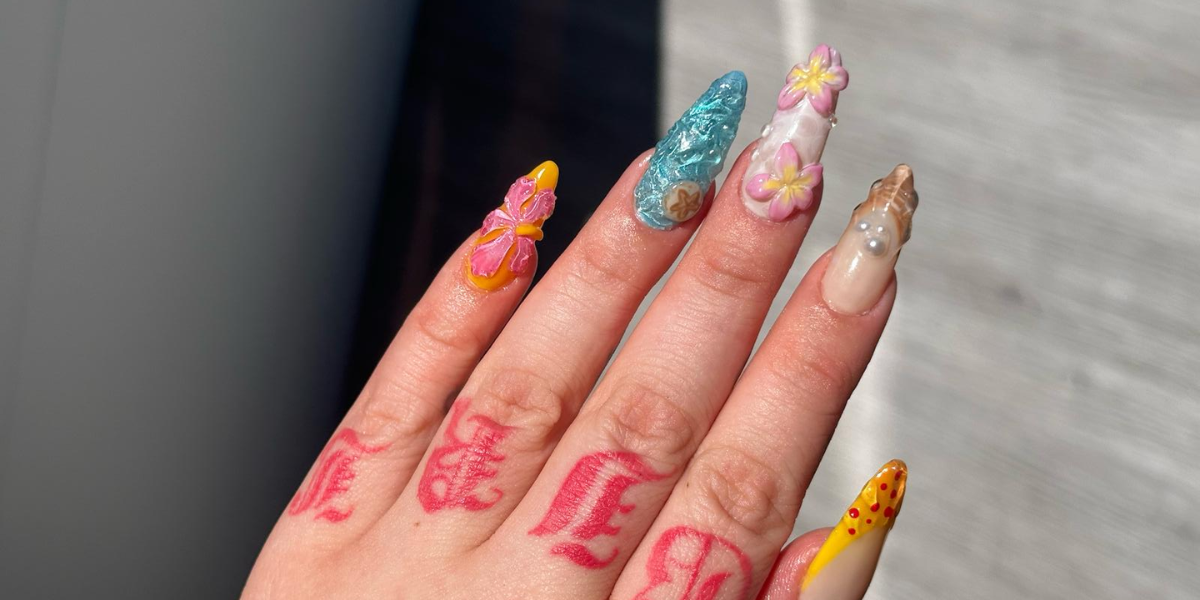 Close-up of colorful 3D floral acrylic nail art with textured ocean-inspired and butterfly designs on a hand.