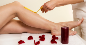 Professional waxing treatment with a client’s legs being measured using a yellow measuring tape, spa towel, rose petals, and candle.