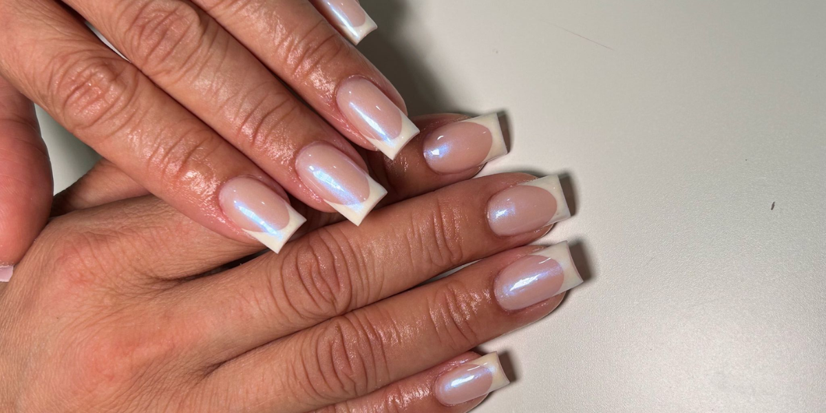 Short nude nails with glossy white French tips and a subtle iridescent shine.