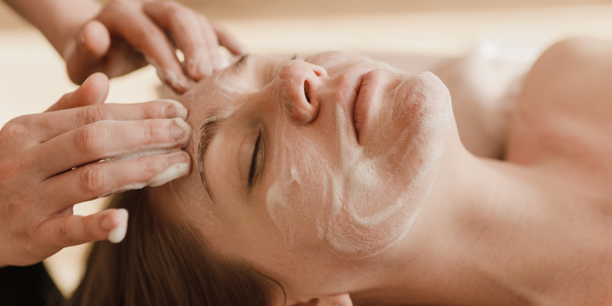 Close-up of a relaxing facial cleansing treatment with foaming cleanser as an esthetician gently massages a client's face during a professional spa skincare session.