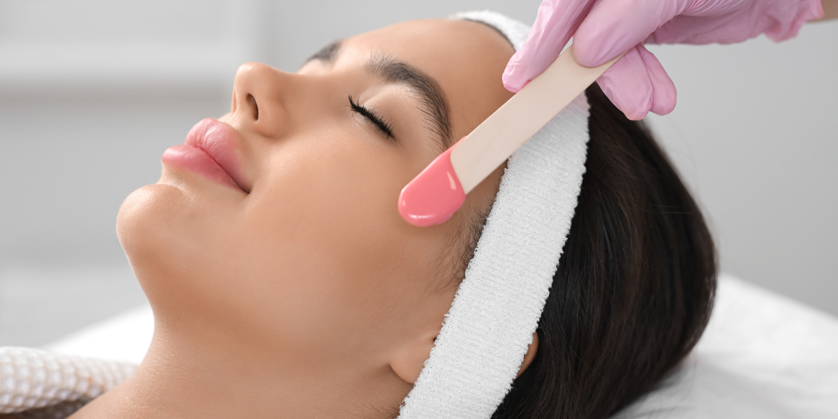 Facial waxing treatment with warm wax applied to a woman’s cheek.